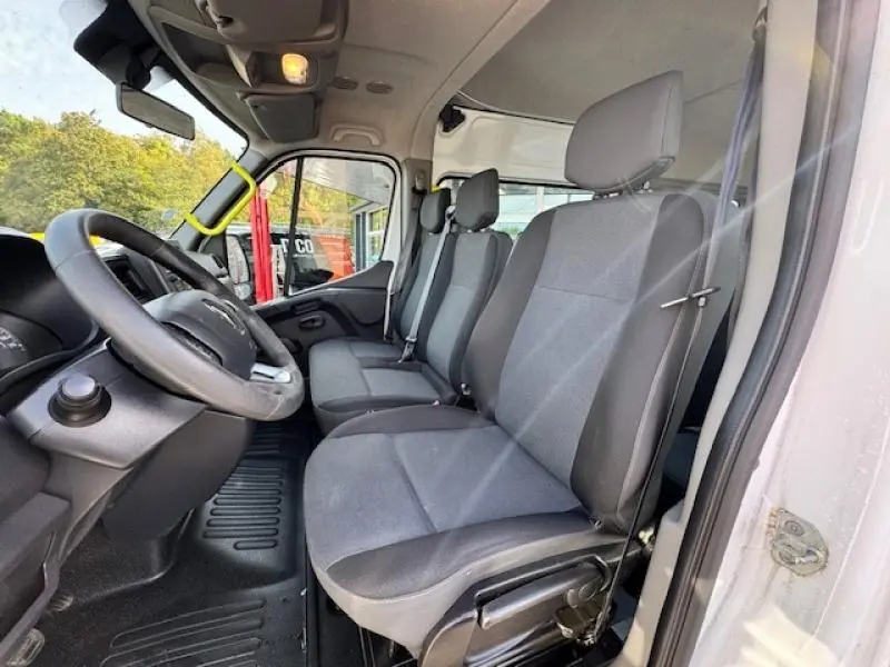 Vue intérieure côté conducteur du Renault Master Combi blanc minéral montrant les sièges avant en tissu gris foncé.