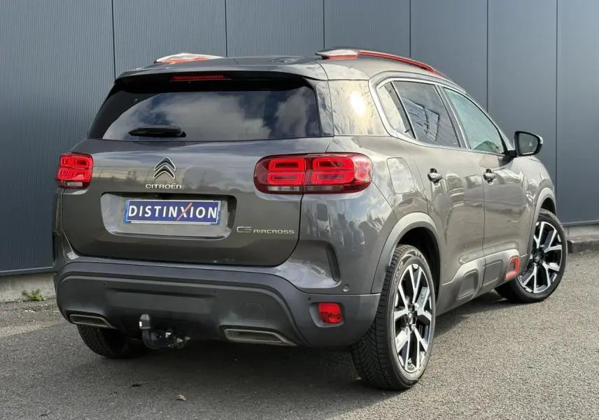 Vue 3/4 arrière droite d'un Citroën C5 Aircross gris Platinium avec jantes alliage et attelage visible.