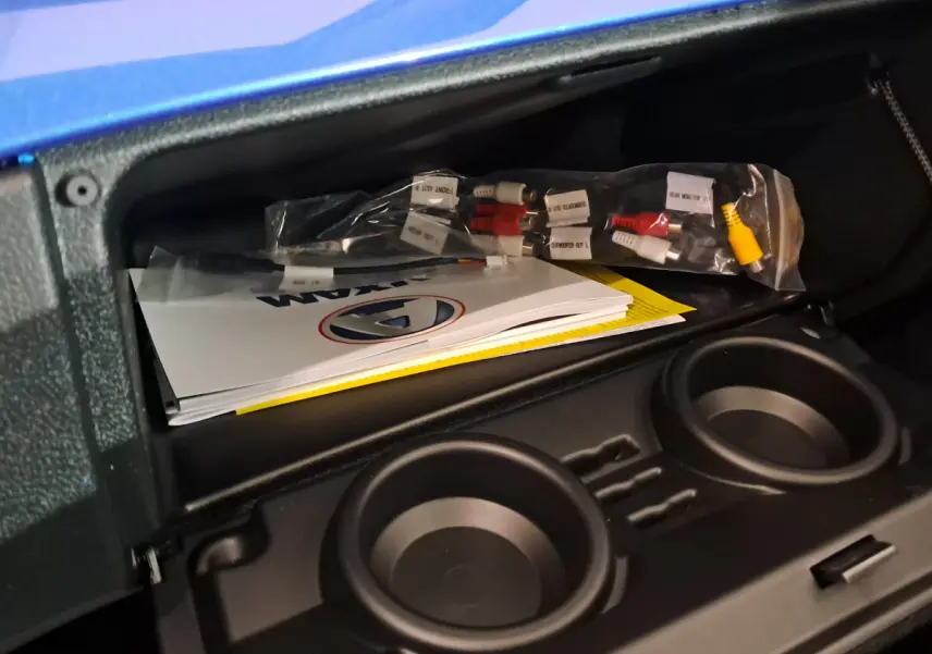 Coffre ouvert de l'AIXAM AMBITION bleu 2026 montrant des manuels et câbles, avec porte-gobelets intégrés.