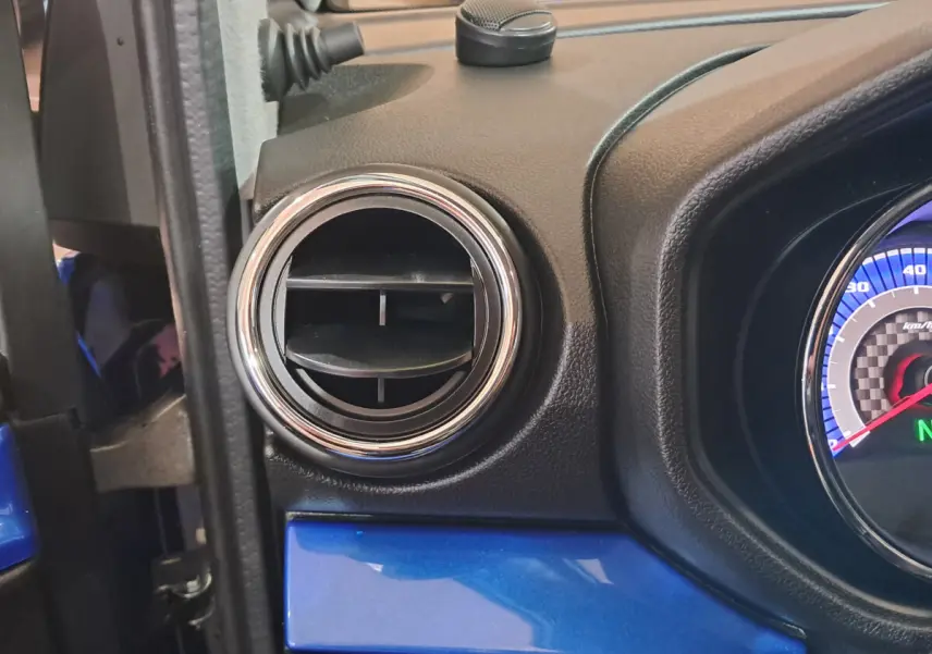 Détail de la ventilation côté gauche du tableau de bord bleu d'une Aixam Ambition 2026 avec compteur partiel visible.