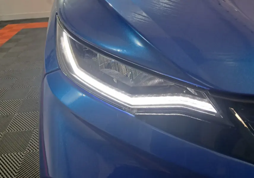 Gros plan sur le phare avant gauche allumé d'une Aixam Ambition bleu métallisé 2026, avec carrosserie lisse et brillante.