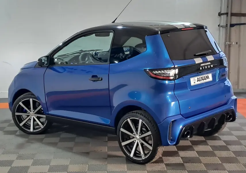 Vue 3/4 arrière droite d'une Aixam Ambition 2026 bleu avec jantes noires et toit noir brillant en intérieur.