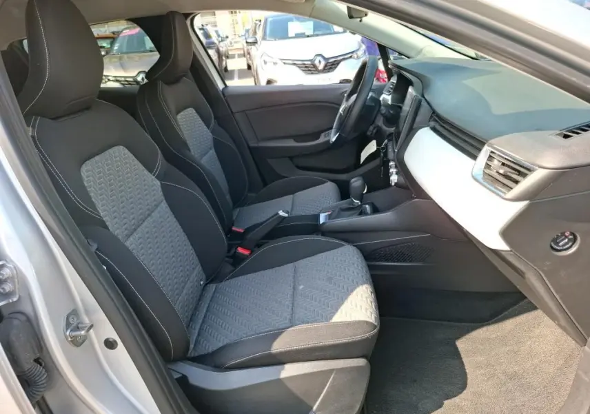 Vue intérieure côté conducteur de la Renault Clio gris platine 2023, sièges tissu bicolore et tableau de bord épuré.