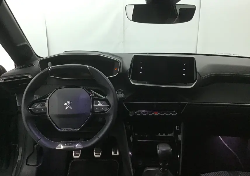 Vue intérieure frontale du tableau de bord noir de la Peugeot 208 1.2 PureTech 100 GT avec volant compact et écran tactile central.