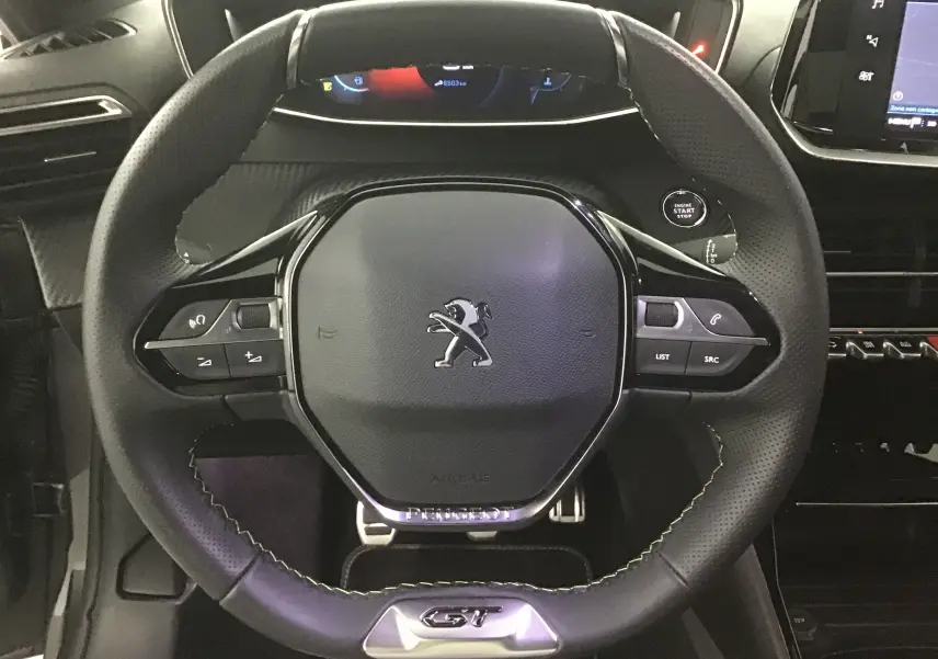 Volant cuir perforé avec logo Peugeot et badge GT, vue rapprochée de l'habitacle d'une 208 1.2 PureTech 2023.