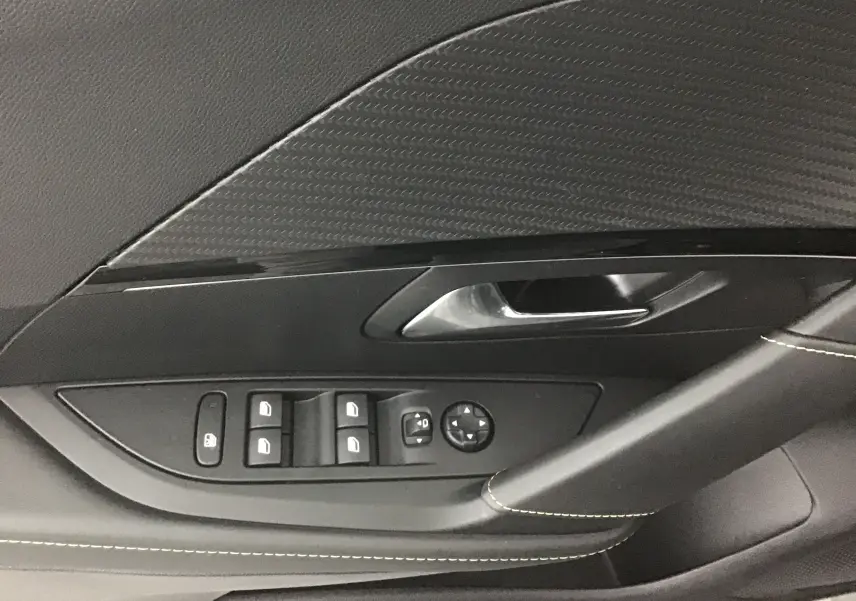 Détail de la porte côté conducteur de la Peugeot 208 1.2 PureTech 100 GT 2023 en gris platinium avec commandes des vitres et rétroviseurs.
