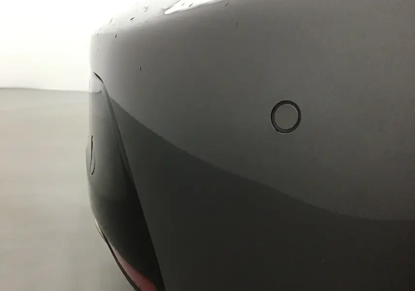 Gros plan sur le pare-chocs arrière gris platinium du Peugeot 208 1.2 PureTech 100 GT avec capteur de recul visible.