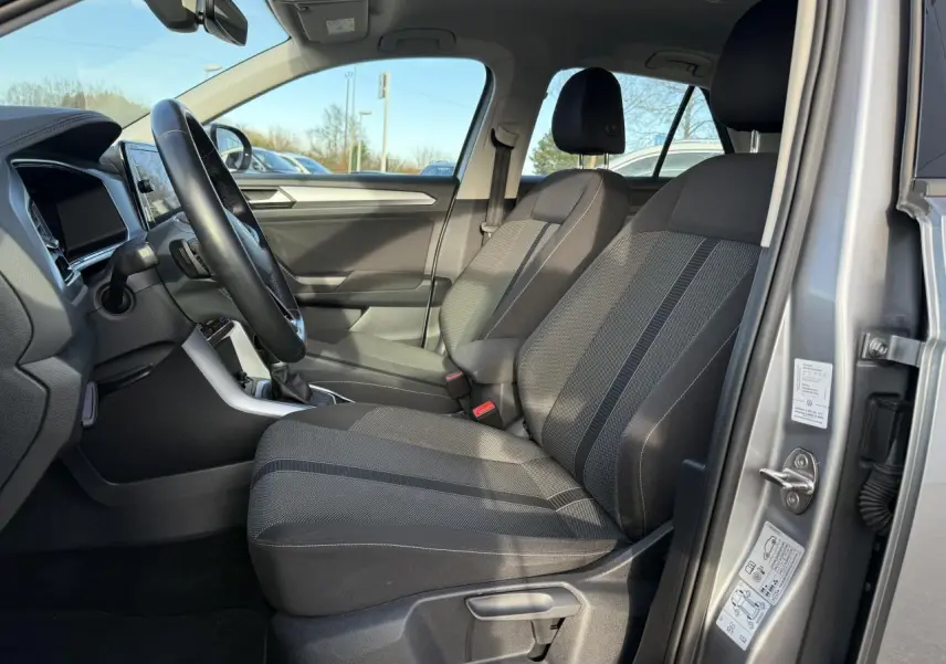 Vue intérieure côté conducteur du Volkswagen T-Roc gris pyrite 2022, montrant les sièges avant et le volant multifonction en cuir.