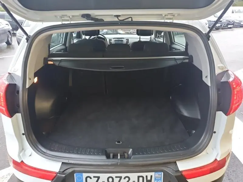 Coffre ouvert vu de l'arrière d'un KIA SPORTAGE blanc, avec cache-bagages et banquette arrière visible.