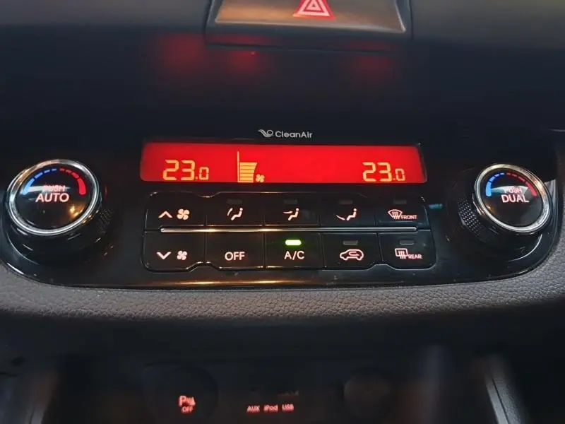 Gros plan sur la console de climatisation digitale rouge du Kia Sportage blanc, avec réglages à 23°C et commandes tactiles.