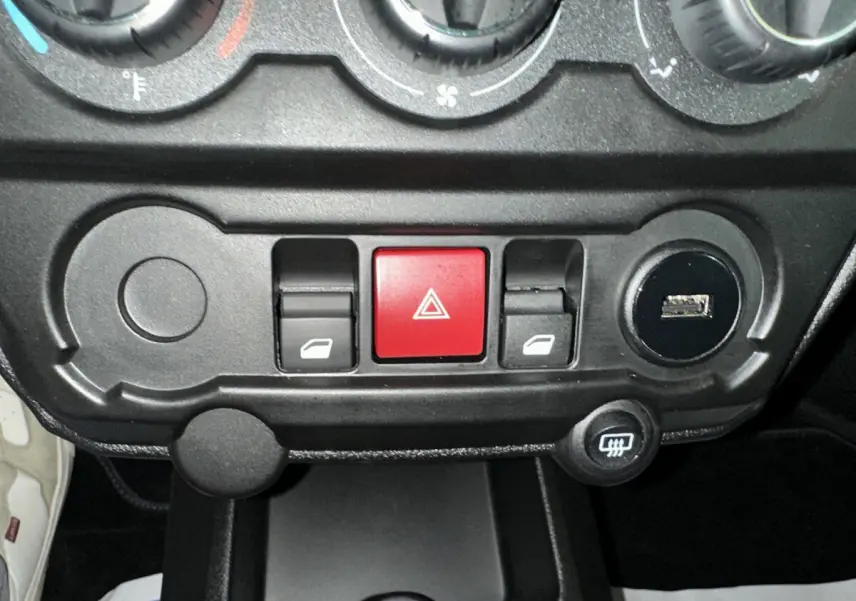 Gros plan sur la console centrale noire de l'AIXAM AMBITION rouge, montrant les commandes de vitres et le bouton de warning rouge.