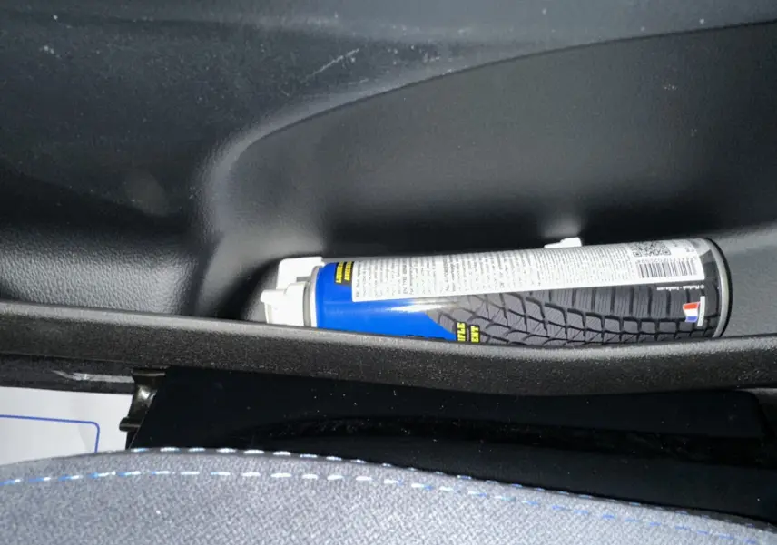 Vue rapprochée de l'intérieur d'une Aixam Ambition rouge 2026, montrant un rangement avec un spray et une couture bleue sur le siège.