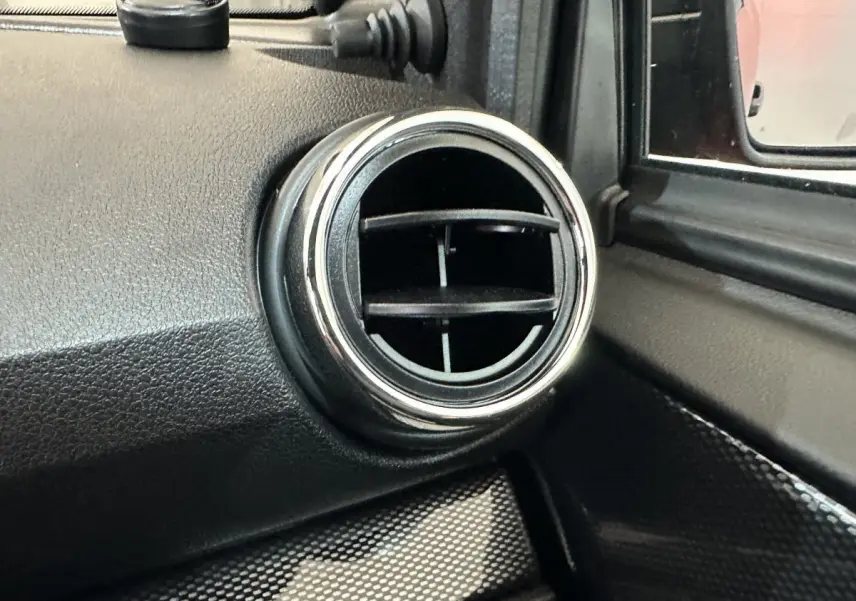 Gros plan sur la sortie d’air ronde chromée côté conducteur de l’AIXAM AMBITION rouge, avec rétroviseur extérieur visible.