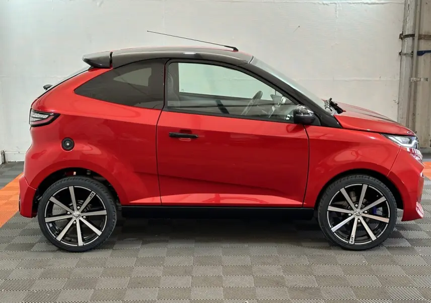 Vue de profil côté gauche d'une Aixam Ambition 0.5 City Coupe GTI rouge avec toit noir et jantes alliage noires.