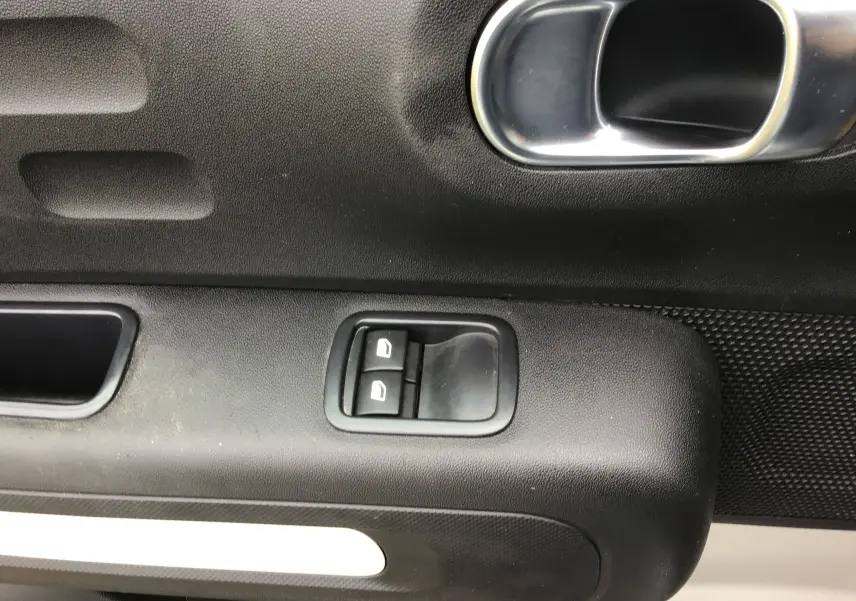 Gros plan sur la commande des vitres électriques côté conducteur d'une Citroën C3 blanche, intérieur noir.