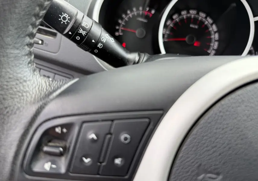 Gros plan sur le volant noir et la manette de commandes d’éclairage du tableau de bord d’une Kia Venga gris 2013.