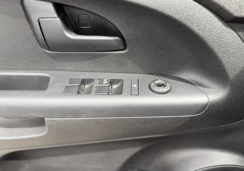 Gros plan sur la commande de porte côté conducteur d’une KIA VENGA gris 2013, avec boutons de vitres électriques et réglage rétroélectrique.