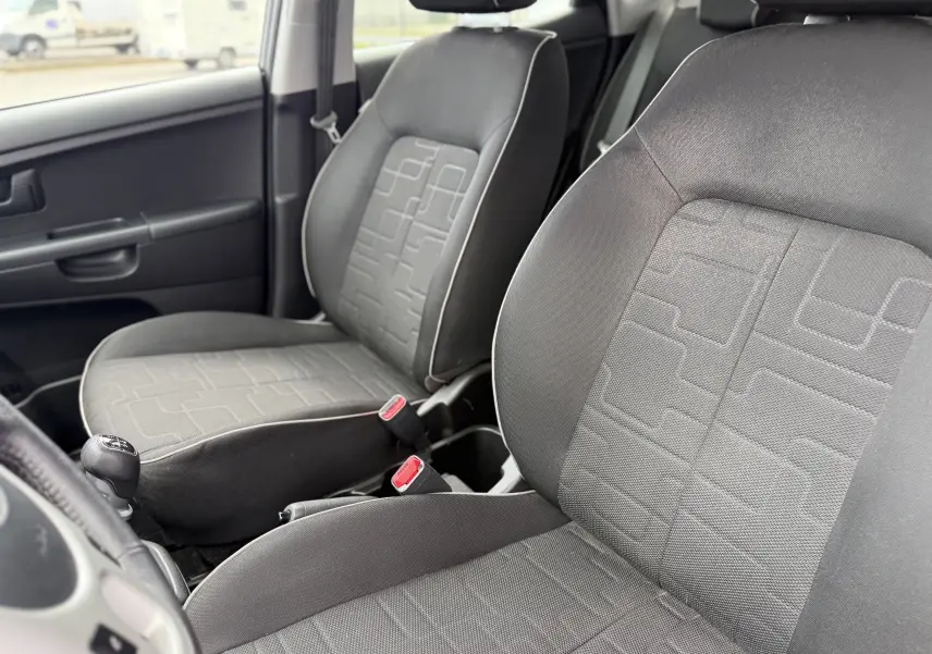 Vue intérieure rapprochée des sièges avant en tissu gris d'une KIA VENGA 1.4 i 90 ACTIVE de 2013 avec boîte manuelle.