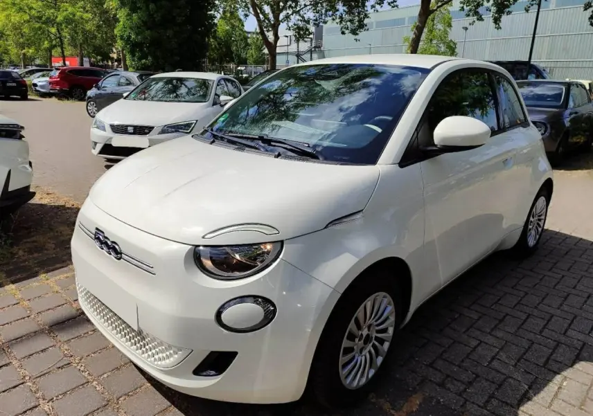 Vue 3/4 avant droite d'une Fiat 500 électrique blanche, avec logo distinctif et jantes multibranches visibles.