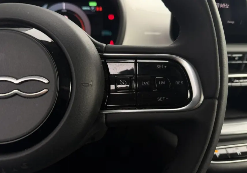 Gros plan sur le volant noir de la Fiat 500 électrique 2024, avec commandes de régulateur de vitesse visibles à droite.