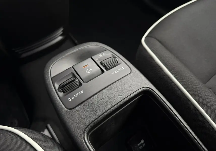 Gros plan sur la console centrale de la Fiat 500 électrique blanche, montrant les commandes e-mode et volume entre les sièges noirs avec surpiqûres blanches.