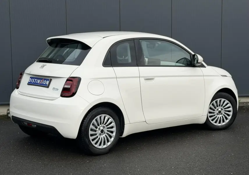 Vue 3/4 arrière droite d'une Fiat 500 électrique blanche 2024 avec porte arrière 3+1 distinctive et jantes multibranches.