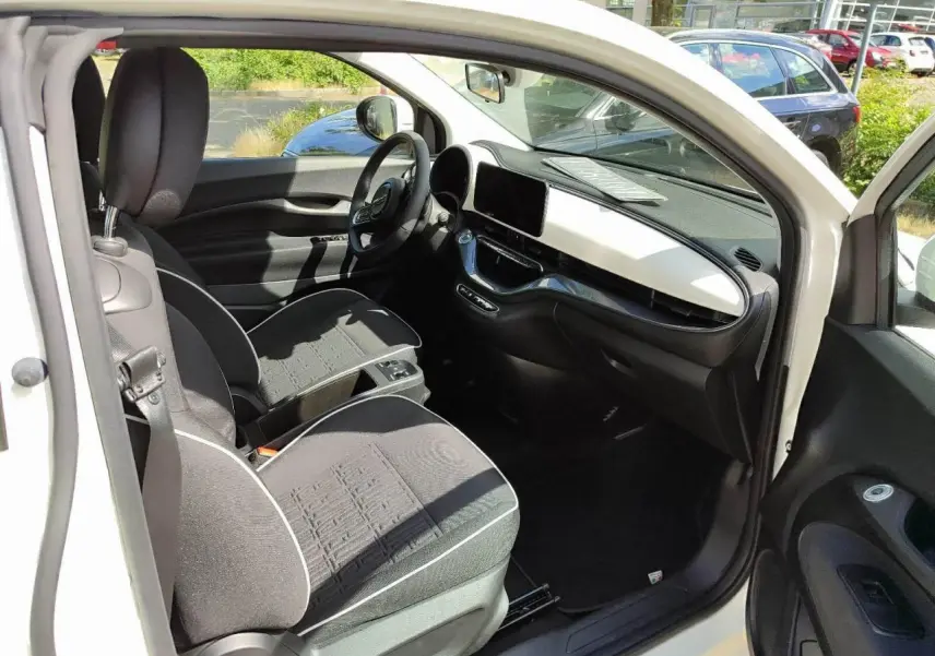 Vue 3/4 avant droite d'une Fiat 500 électrique blanche avec calandre épurée et jantes multibranches.