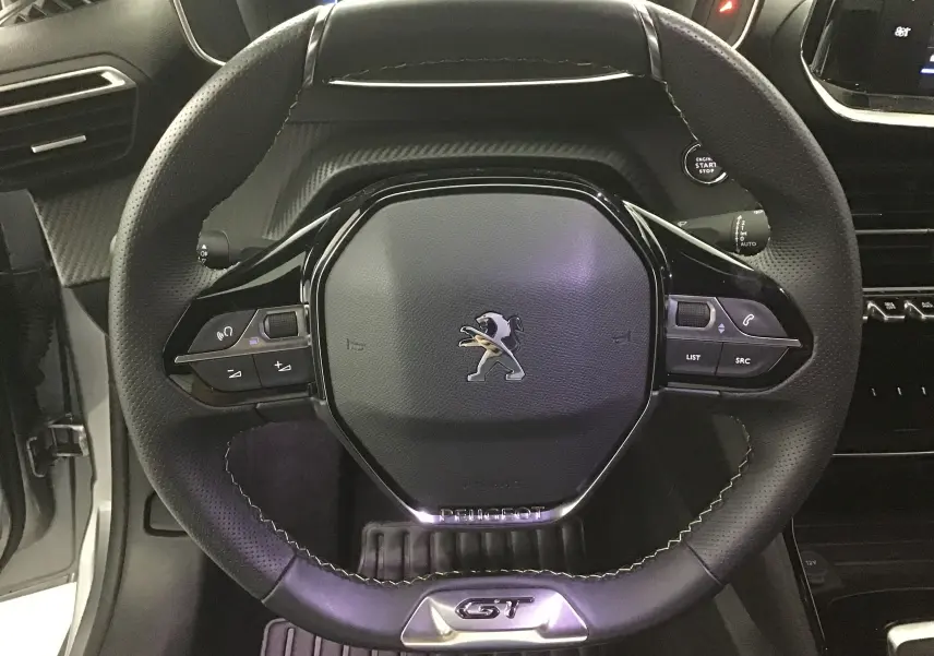 Volant cuir noir avec logo Peugeot et badge GT en vue frontale dans l'habitacle d'une 208 Gris Artense 2023