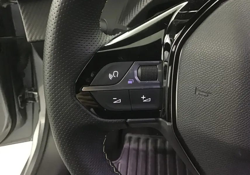 Gros plan sur les commandes gauche du volant en cuir perforé de la Peugeot 208 gris Artense/Noir 2023.