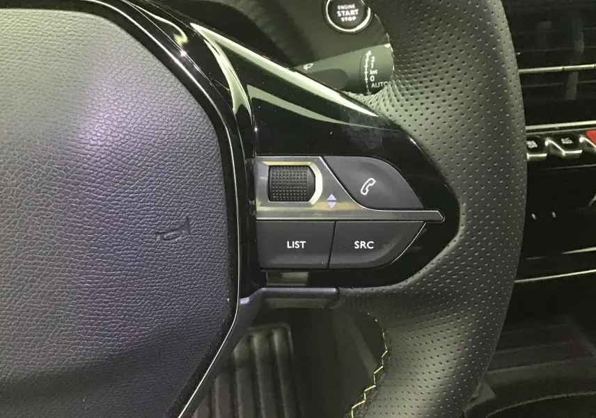 Gros plan sur le côté droit du volant cuir perforé de la Peugeot 208 gris Artense, avec commandes audio et téléphone.