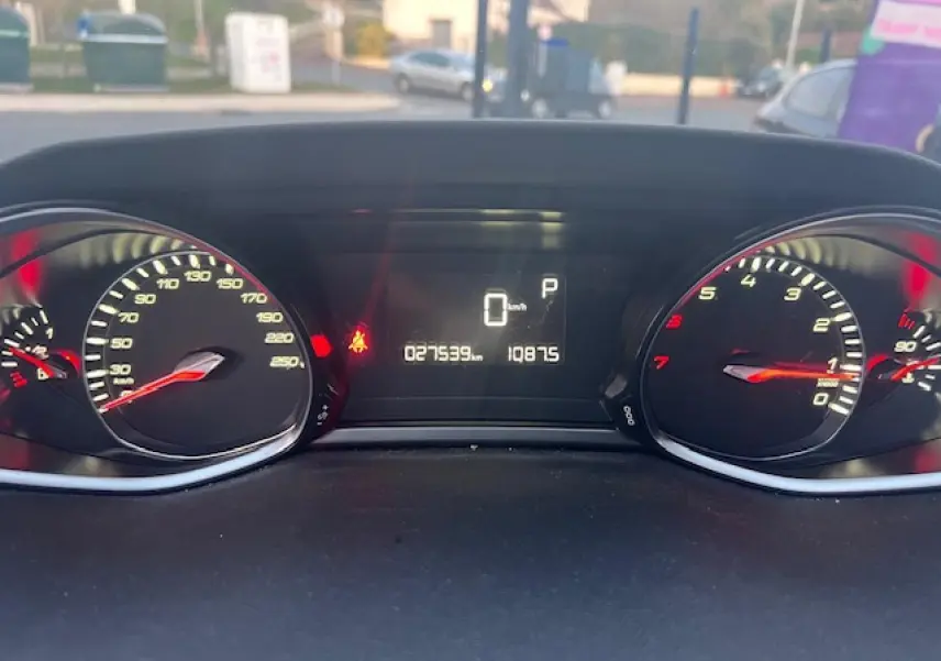 Vue rapprochée du tableau de bord numérique de la Peugeot 308 blanche, affichant 27539 km et indicateurs allumés.