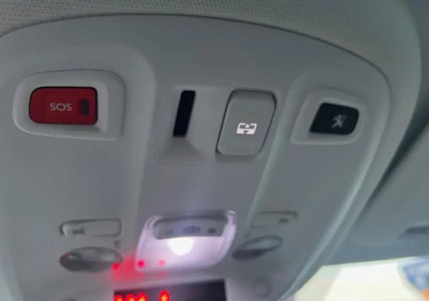 Vue en gros plan du panneau de commandes au plafond intérieur du Peugeot 308 blanc, avec bouton SOS rouge et éclairage blanc.