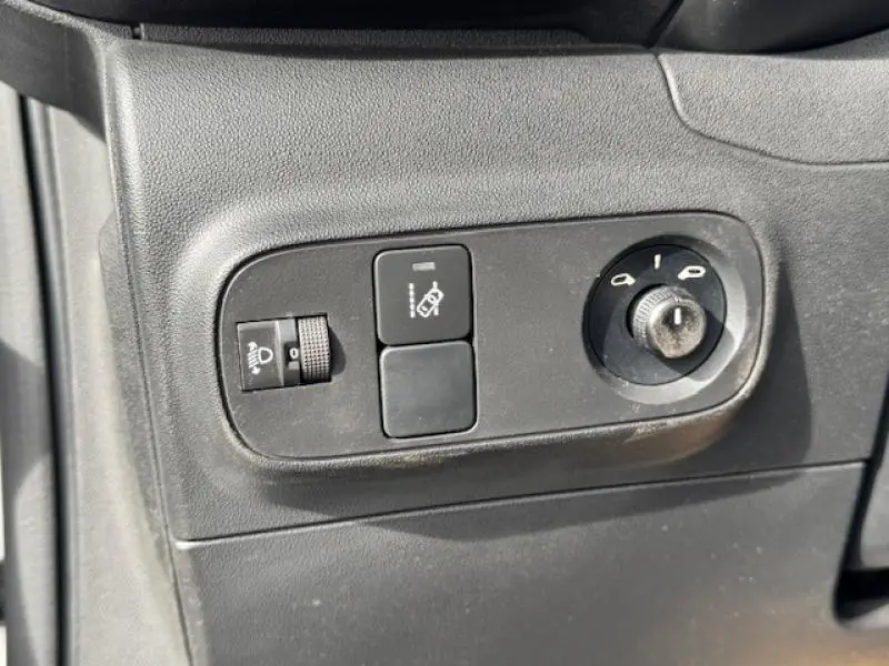 Gros plan sur les commandes noires de réglage des phares et des rétroviseurs d'une Citroën C3 blanche.