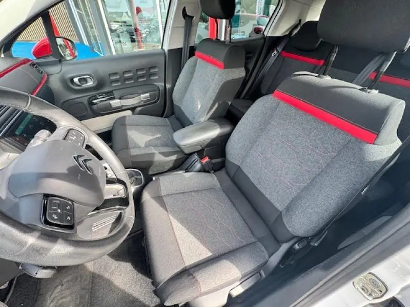 Vue intérieure côté conducteur de la Citroën C3 2017, sièges gris avec bande rouge et volant cuir noir.