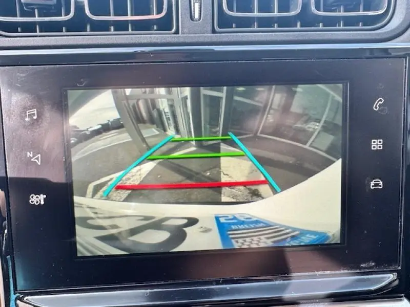 Vue de la caméra de recul de la Citroën C3 blanche, affichant les lignes de guidage colorées sur l'écran tactile.