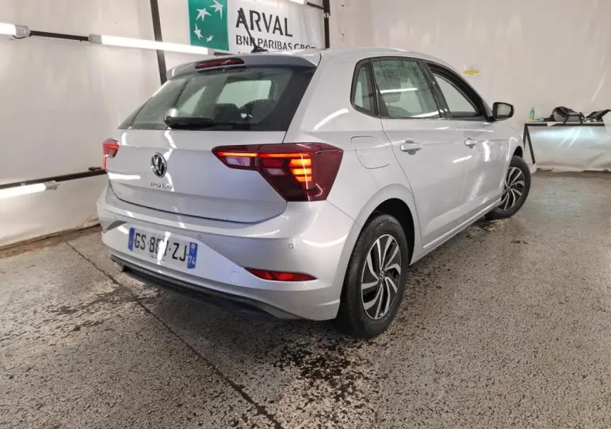 Vue 3/4 arrière droite d'une Volkswagen Polo gris clair avec feux arrière allumés dans un garage.