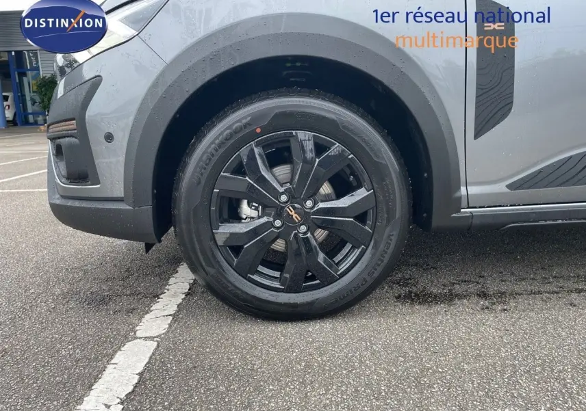 Gros plan sur la roue avant gauche noire et la partie basse grise schiste métallisée d'une Dacia Sandero Stepway 2024.