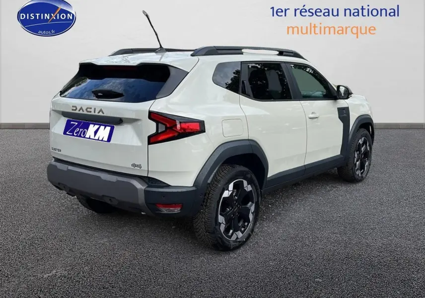 Vue 3/4 arrière droite du Dacia Duster 2025 couleur Sandstone avec barres de toit et jantes alu noires.