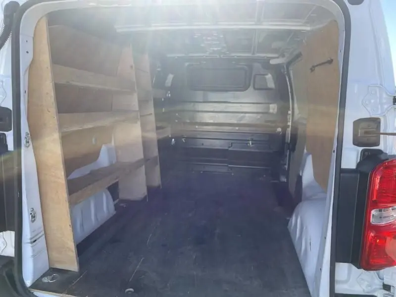 Intérieur du fourgon blanc Peugeot Expert 2023 vu de l'arrière, avec étagères en bois sur le côté gauche.