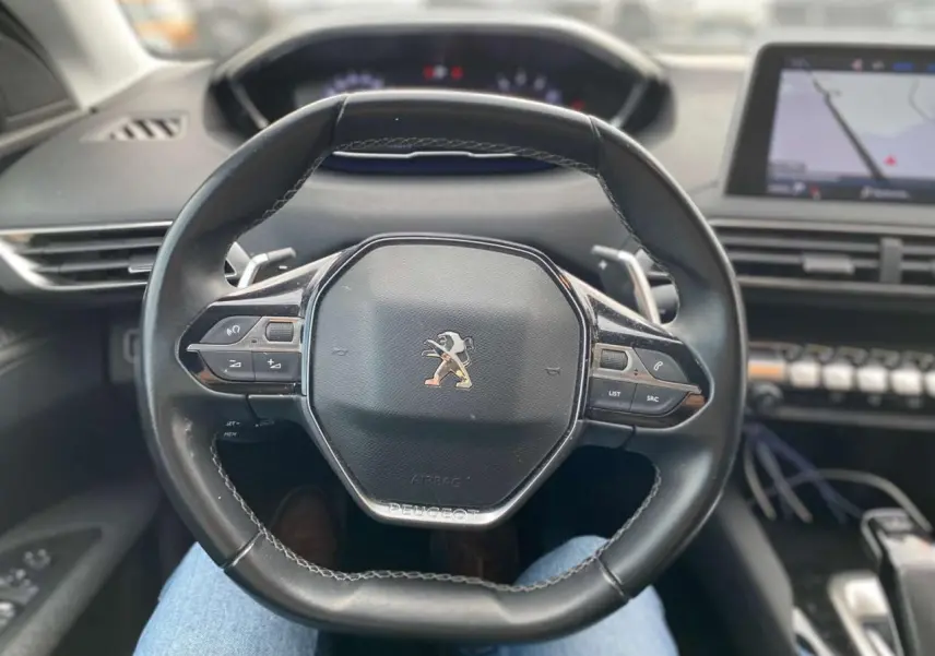 Vue intérieure centrée sur le volant cuir du Peugeot 3008 noir, avec tableau de bord et écran de navigation visibles.
