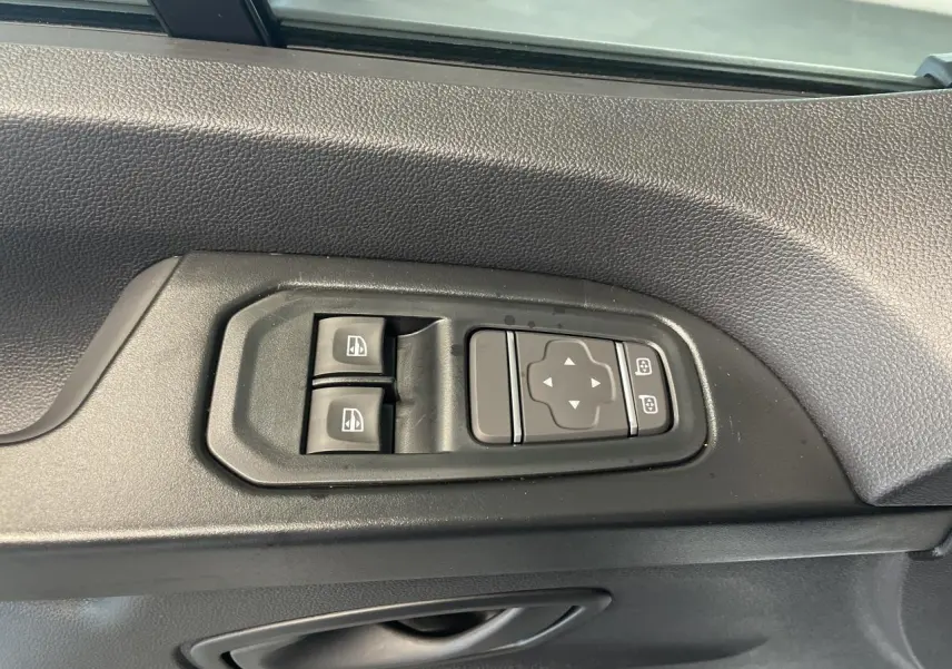 Gros plan sur les commandes de lève-vitres et réglage des rétroviseurs côté conducteur du Renault Trafic blanc.