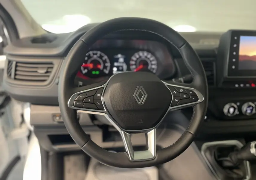 Vue centrée sur le volant noir du Renault Trafic Fourgon blanc, avec tableau de bord et écran tactile en arrière-plan.