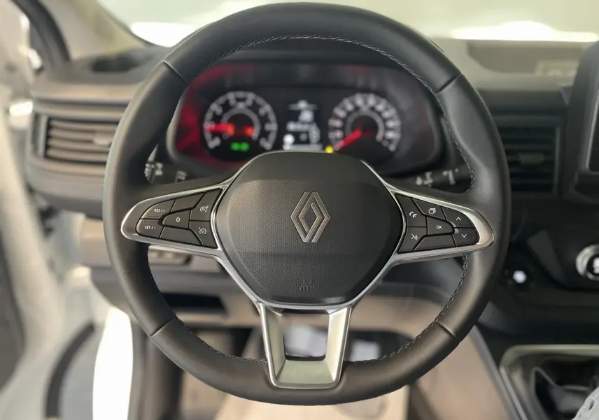 Volant noir avec logo Renault au centre, cadrans de tableau de bord flous en arrière-plan, intérieur du Renault Trafic Fourgon.