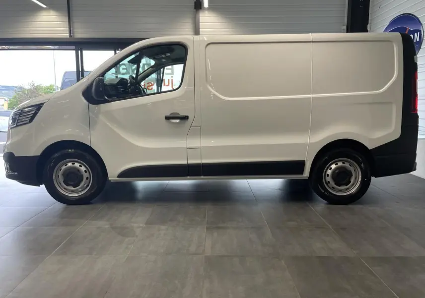 Profil droit du Renault Trafic Fourgon blanc 2025 avec jantes tôles et porte latérale coulissante visible en intérieur showroom.