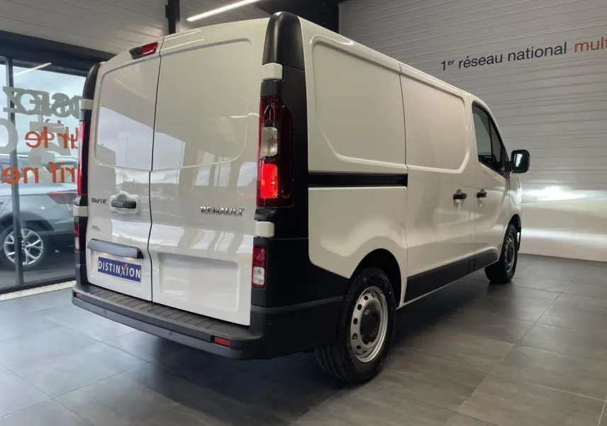 Renault Trafic Fourgon blanc en vue 3/4 arrière droit, avec feux arrière allumés et jantes tôles 16 pouces.
