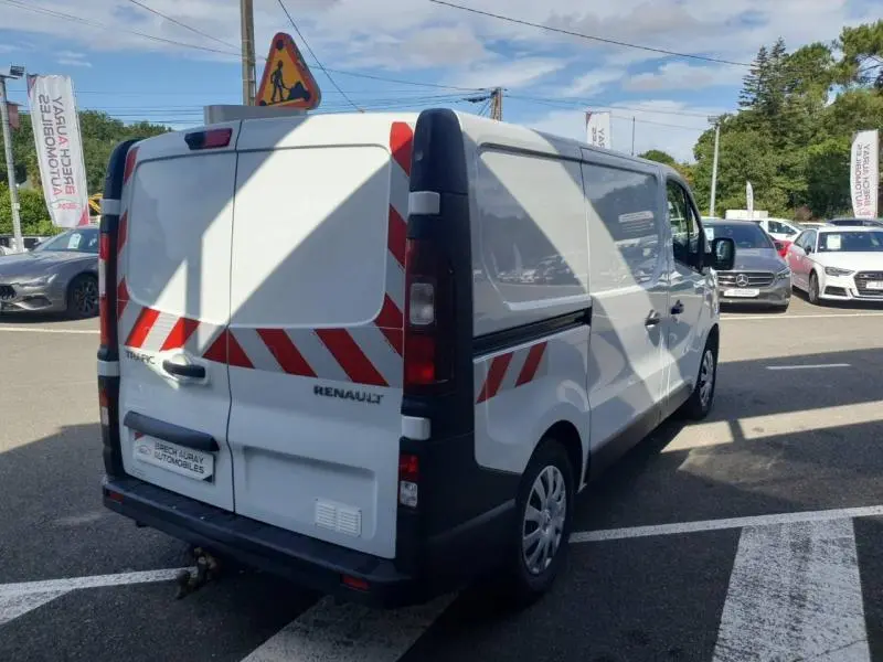 Renault Trafic Fourgon blanc glacier vu en 3/4 arrière droit avec bandes réfléchissantes rouges et blanches sur les portes arrière.