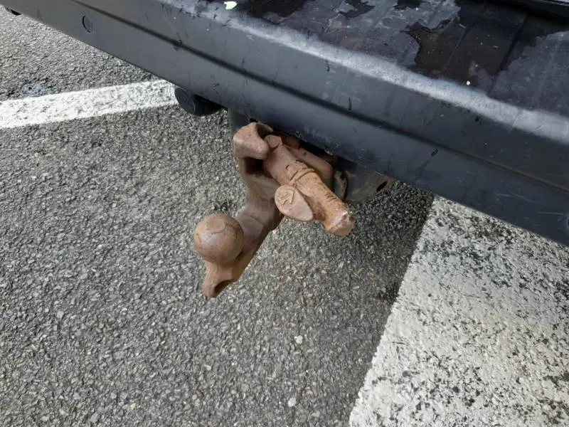 Gros plan sur l'attelage rouillé sous le pare-chocs arrière noir d'un Renault Trafic Fourgon blanc glacier.