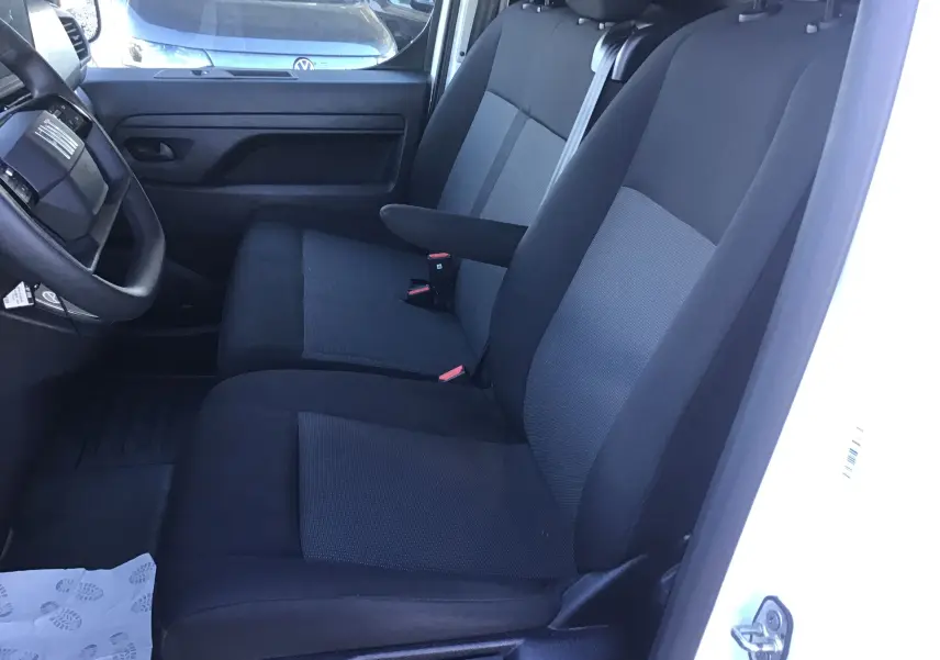 Vue intérieure côté conducteur du FIAT Scudo Fourgon blanc 2024, sièges avant en tissu noir et gris avec accoudoir.