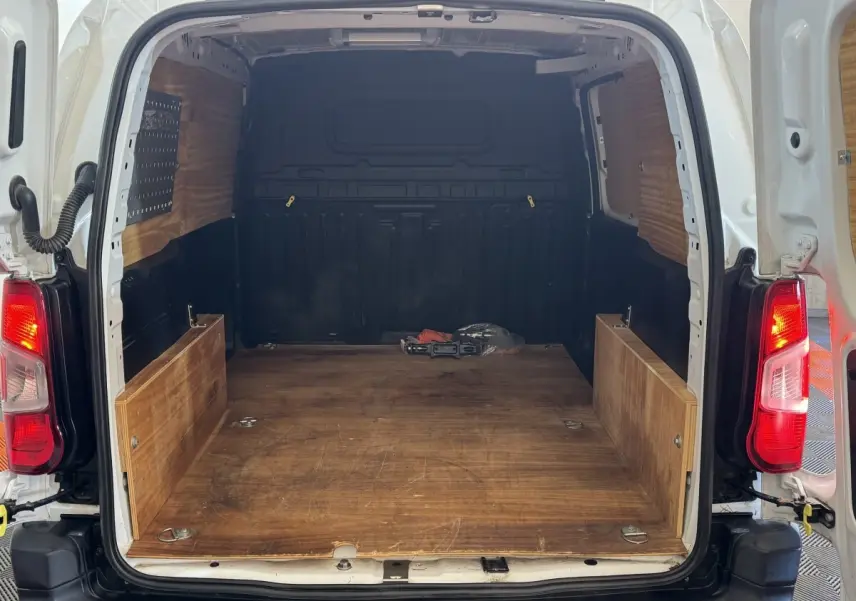 Vue arrière ouverte du Citroën Berlingo blanc 2020 montrant l'espace de chargement en bois et les feux arrière allumés.