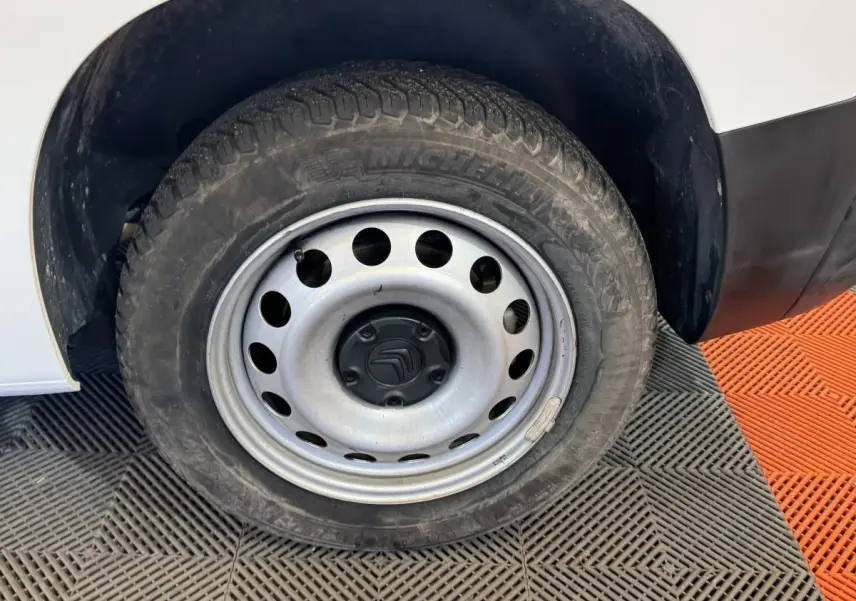 Gros plan sur la roue avant gauche en jante acier du Citroën Berlingo blanc, avec pneu Michelin visible.